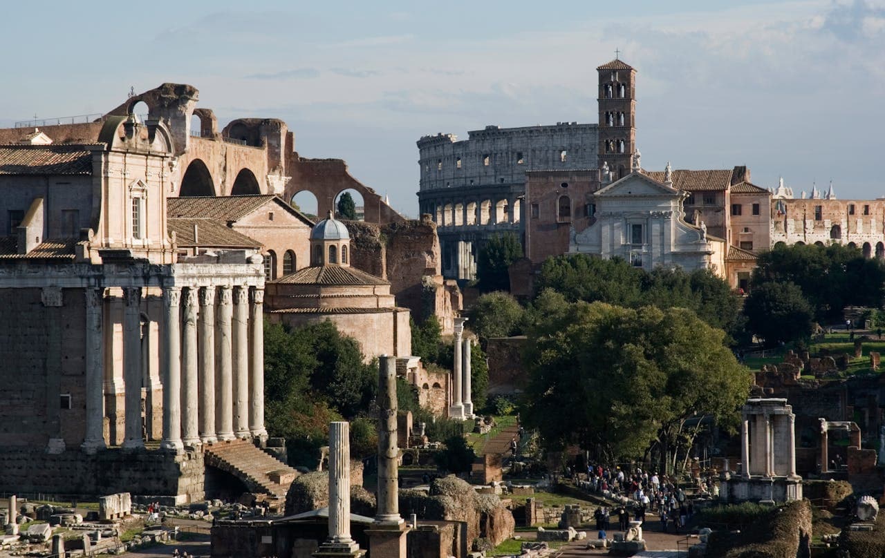 Panoramic view of the Roman Forum with ancient ruins, temples, and the Colosseum in the background on a sunny day in Rome, Italy.